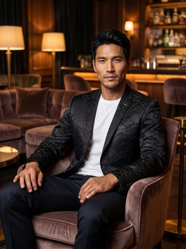 This tailored black blazer features a sophisticated satin-finish fabric with a textured, geometric jacquard pattern. It is designed with notched lapels, a single-breasted two-button closure, and functional flap pockets, offering a modern twist on classic 