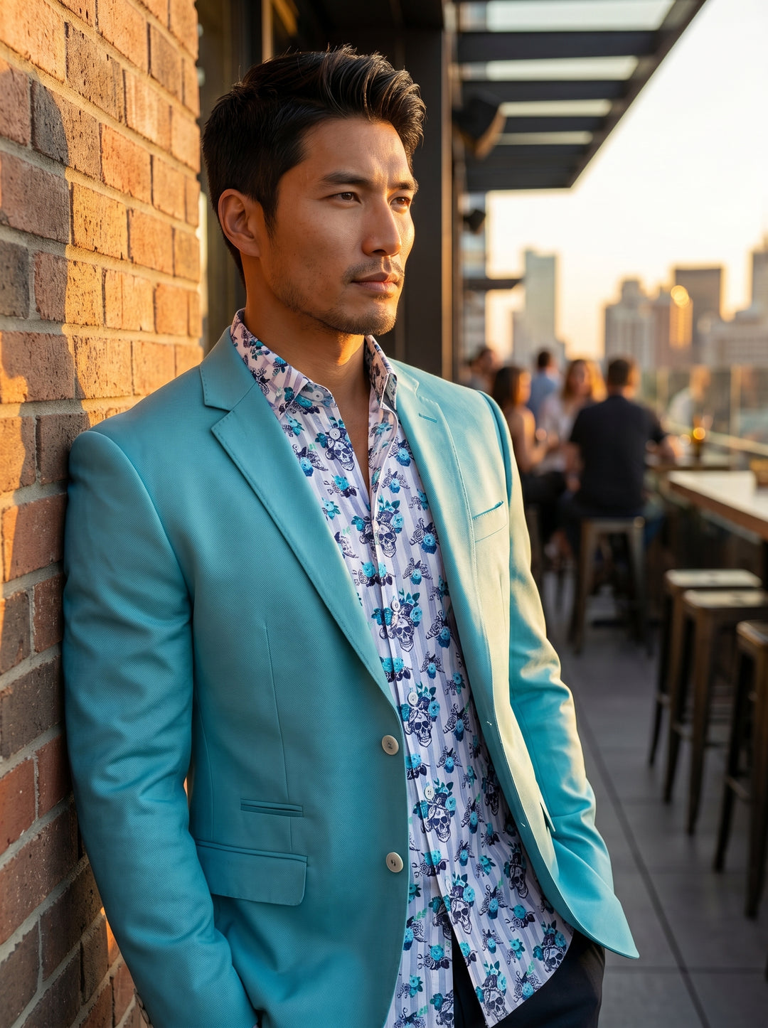 A vibrant turquoise two-button blazer with a notch lapel and flap pockets, layered over a white button-down shirt featuring blue floral and skull motifs. The ensemble offers a bold, contemporary take on smart-casual attire with high-quality tailoring and 
