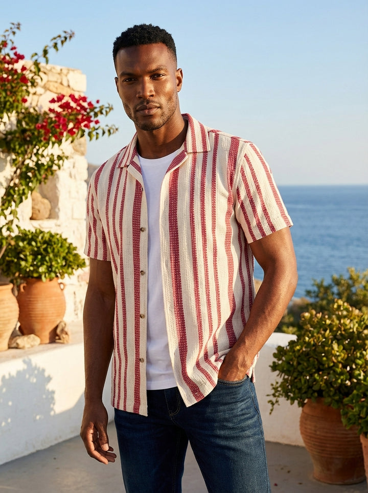 This short-sleeved button-down features a sophisticated textured fabric with classic vertical red stripes on an off-white base. Designed with a clean-cut camp collar, it offers a versatile layering option for a smart-casual look that balances modern style