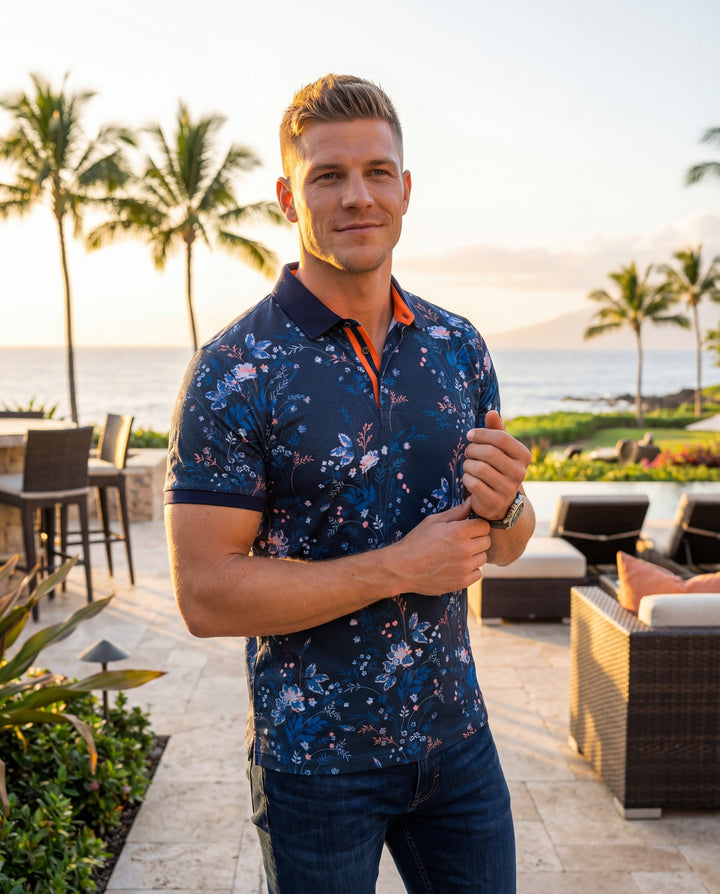 This sophisticated navy blue polo shirt features an intricate all-over botanical print with vibrant pink and light blue floral accents. Crafted with a tailored fit, it includes a classic collar with contrasting orange inner trim and matching ribbed sleeve