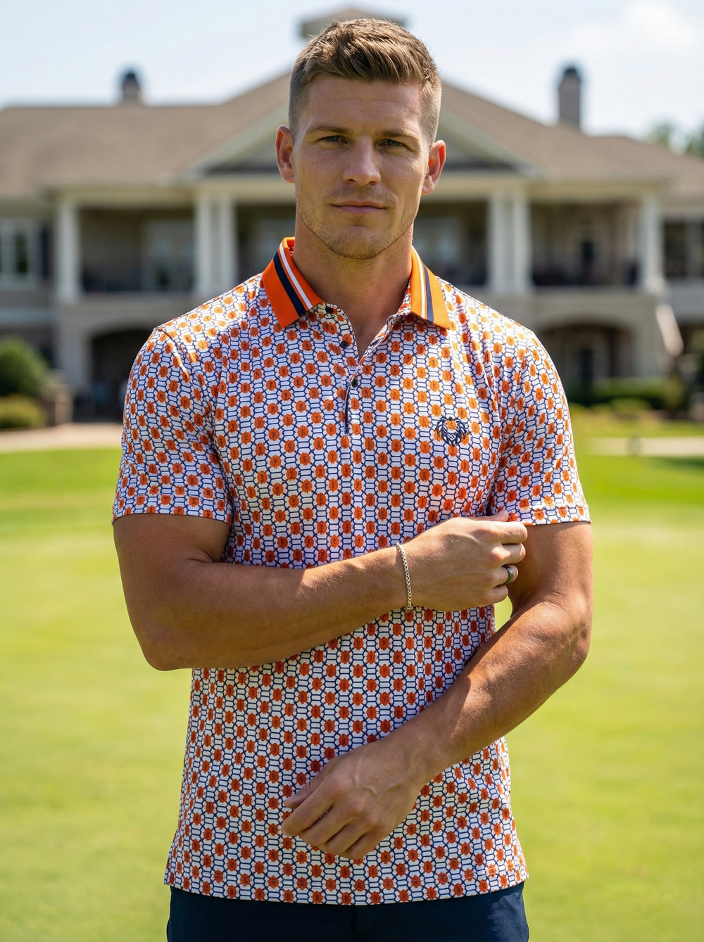 This men's short-sleeve polo shirt features a vibrant geometric link pattern in orange and white. It is accented by a bold orange collar with navy stripes, a two-button placket, and a distinct chest logo for a sophisticated athletic look.