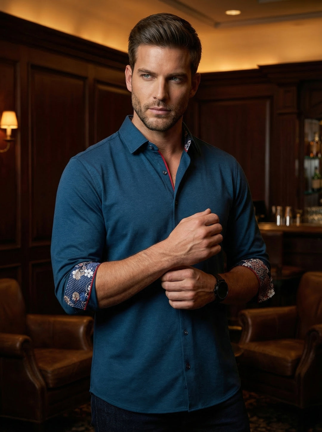 This sophisticated men's button-down shirt features a deep teal hue and refined jersey-knit texture. Red piping along the placket and intricate floral-patterned cuff linings provide a vibrant contrast, making it an ideal choice for a sharp, modern evening