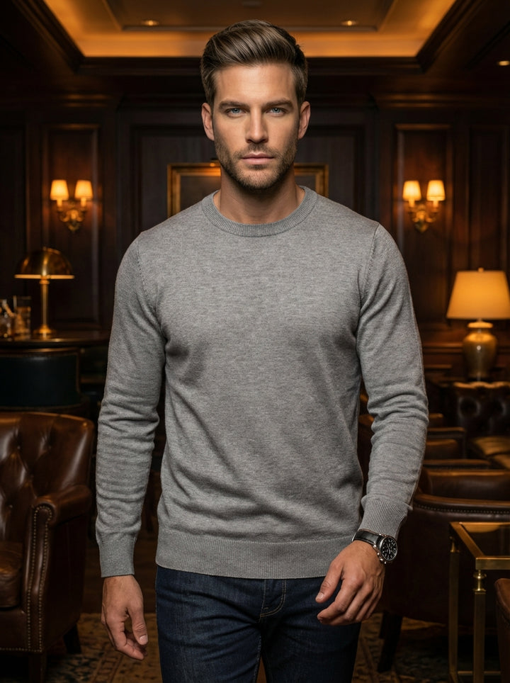A premium heather grey crewneck sweater featuring a fine-knit texture and ribbed cuffs for a tailored fit. This versatile garment offers a sophisticated silhouette perfect for layering or wearing alone, paired with dark denim and a classic aviator-style c