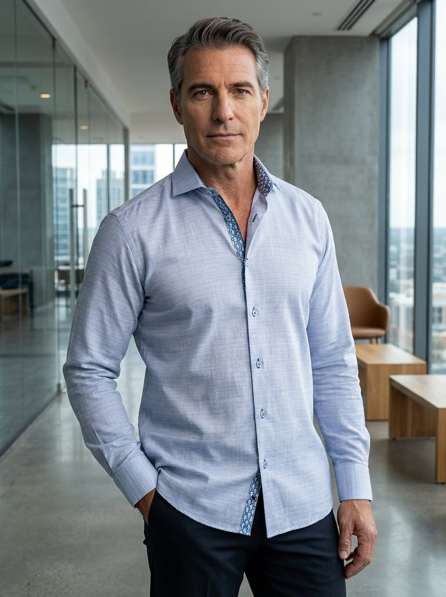 This light blue long-sleeved dress shirt features a textured micro-pattern and a sophisticated spread collar. It includes a contrasting geometric print inside the collar and placket for a modern touch, paired with dark buttons and a refined, tailored fit.