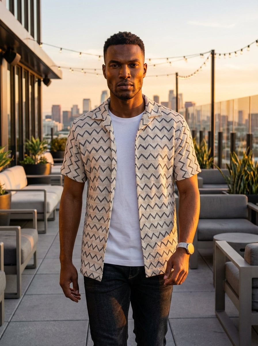 This short-sleeved knit shirt features a striking monochromatic zigzag pattern. The cream-colored textured fabric offers a relaxed yet sophisticated look, featuring a camp collar and an open front perfect for layering over a crisp white tee and dark denim