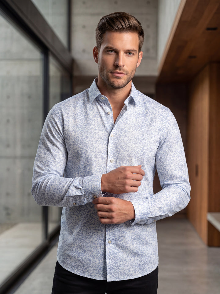 This men's long-sleeve button-down shirt features an intricate light blue botanical leaf pattern on a crisp white background. It offers a modern tailored fit with a classic collar and pearlescent buttons, perfect for elevating casual looks with sophistica