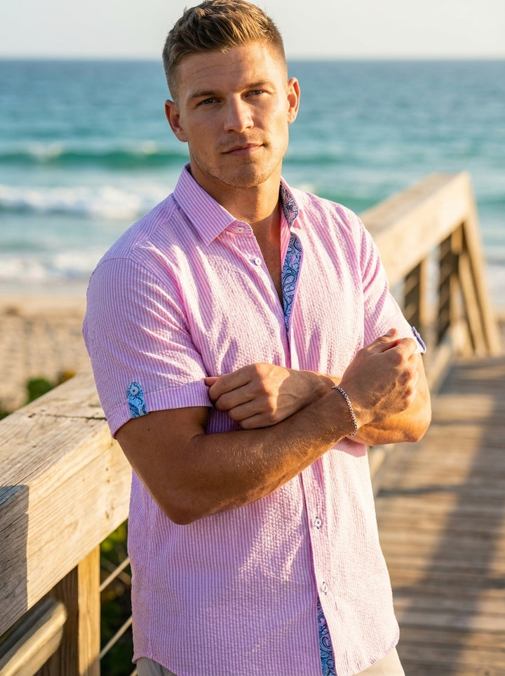 This men's short-sleeve button-down features a vibrant pink and white seersucker stripe. It is designed with a classic collar, contrast patterned trim on the inner placket and sleeve cuffs, and a tailored fit perfect for stylish warm-weather occasions.