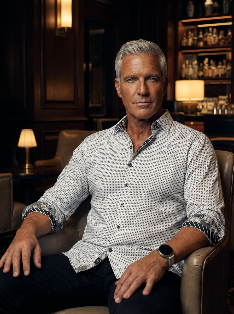 This men's long-sleeve dress shirt features a crisp white base adorned with a meticulous black geometric micro-dot pattern. The design is elevated by contrasting floral and striped trims on the inner collar and cuffs, creating a sophisticated, modern aest