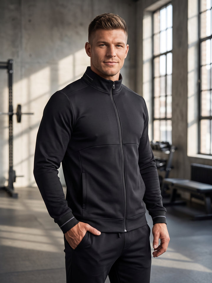 This sleek men's zip-up jacket in matte black features a high mock-neck collar and subtle grey piping on the cuffs and neck. Designed with a tailored fit and paneled construction, it offers a sophisticated athletic look for versatile layering.