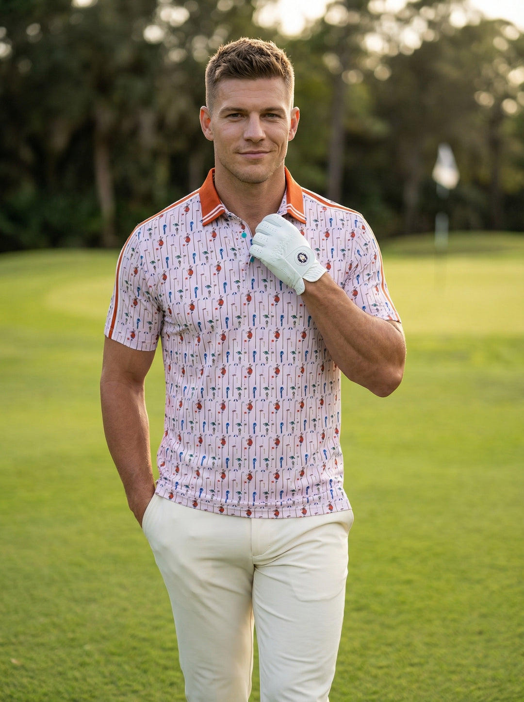 This light pink performance polo features an all-over golf motif including bags, clubs, and flags. It is accented with a burnt orange tipped collar, matching shoulder stripes, and a teal interior placket, offering a playful twist on classic athletic wear.