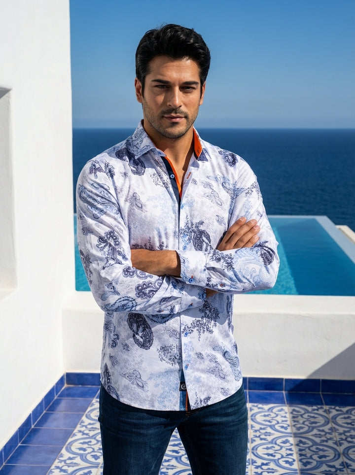 This sophisticated long-sleeve white button-down shirt features an intricate blue paisley and floral motif. Detailed with contrasting orange and navy trim inside the collar and cuffs, it offers a refined yet artistic look, paired here with dark denim jean