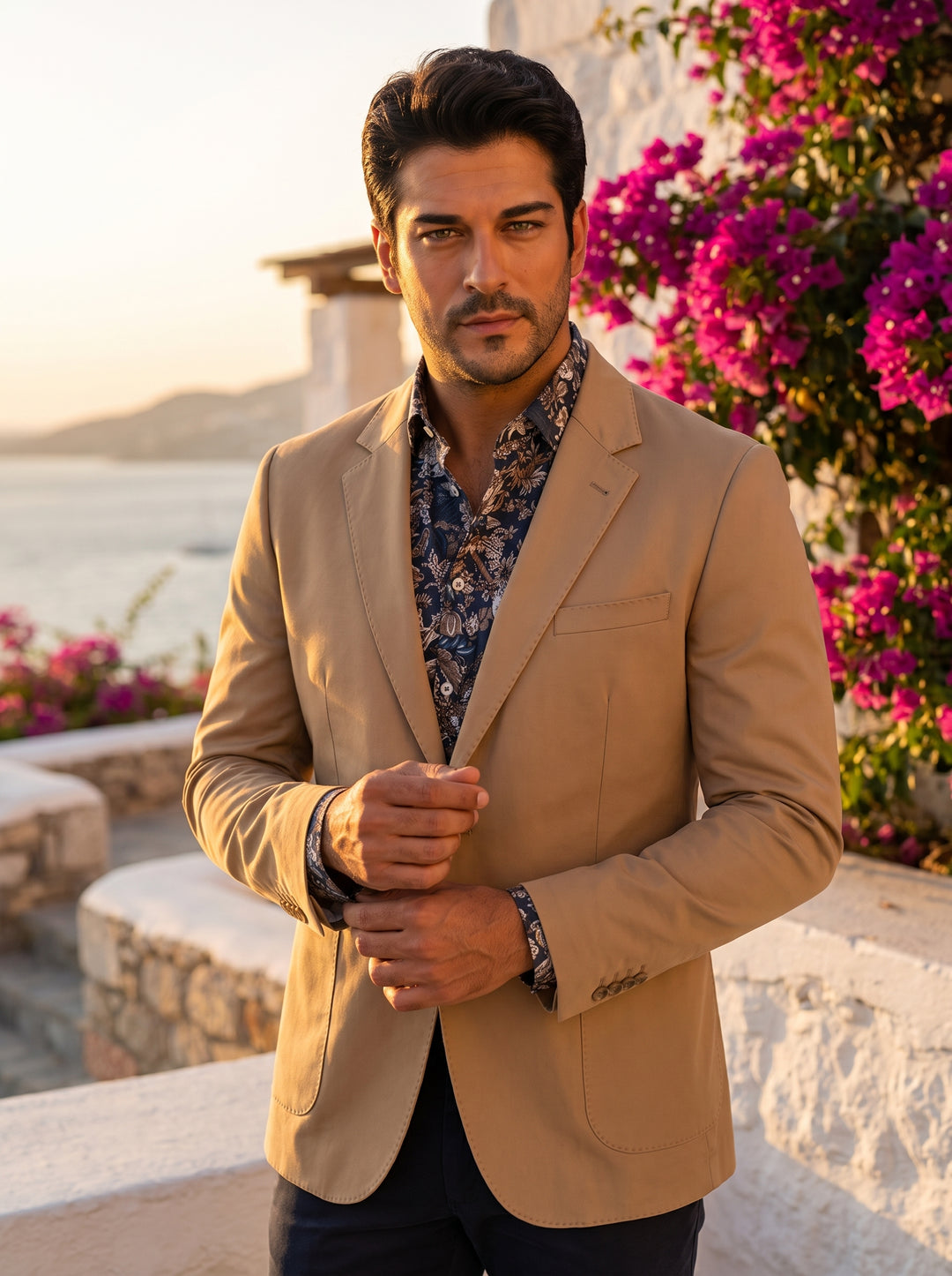 This tailored camel blazer features a classic two-button closure, notched lapels, and rounded patch pockets for a relaxed yet refined look. Made from a smooth cotton blend, it is paired here with a vibrant navy and brown floral patterned shirt.
