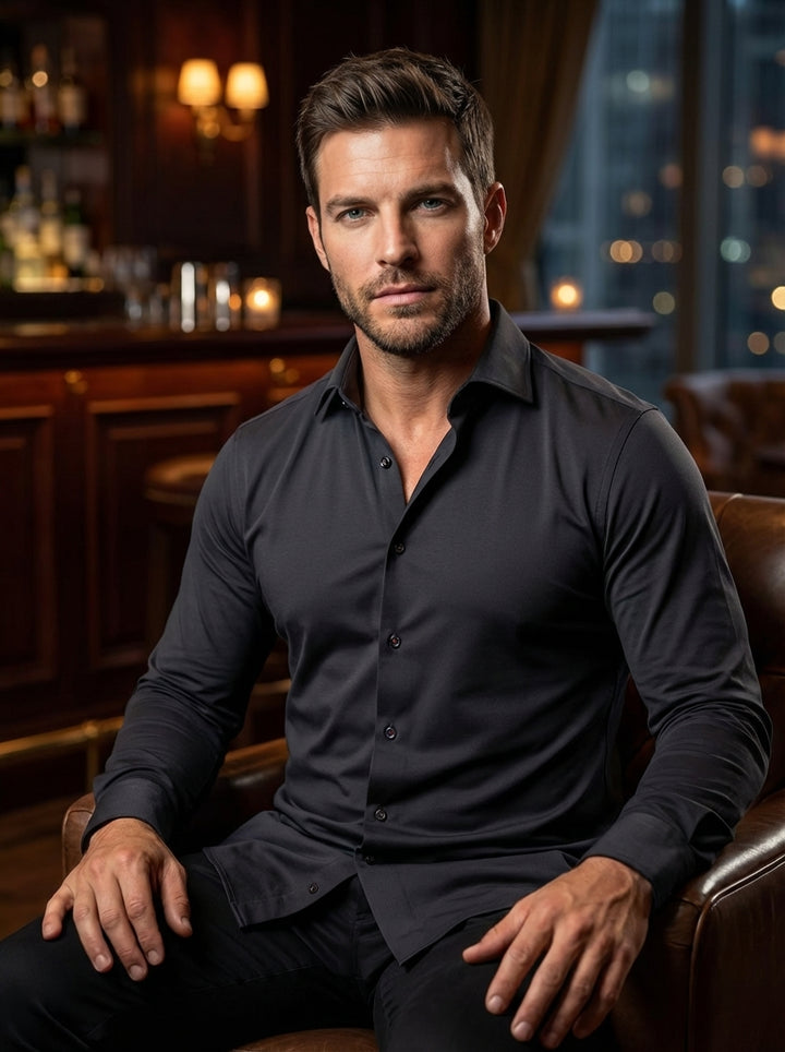 This sleek, charcoal black long-sleeve button-down shirt is crafted from a high-performance, stretch-knit fabric for a modern, slim fit. It features a sophisticated spread collar, subtle dark buttons, and a curved hem, making it ideal for transitioning fr