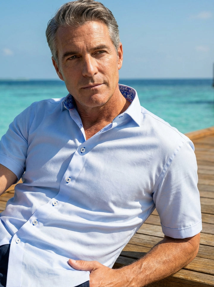 This Masutto short-sleeved button-down shirt features a crisp light blue fabric accented by a vibrant paisley pattern on the inner collar. Design details include white buttons with blue thread and a structured collar for a refined yet casual look.