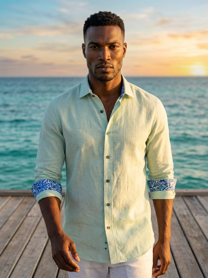 This sophisticated pale mint green linen button-down shirt offers a breathable, textured feel perfect for warm climates. It features a unique contrasting blue floral pattern on the inner collar and cuffs, adding a modern, decorative touch to a classic sil