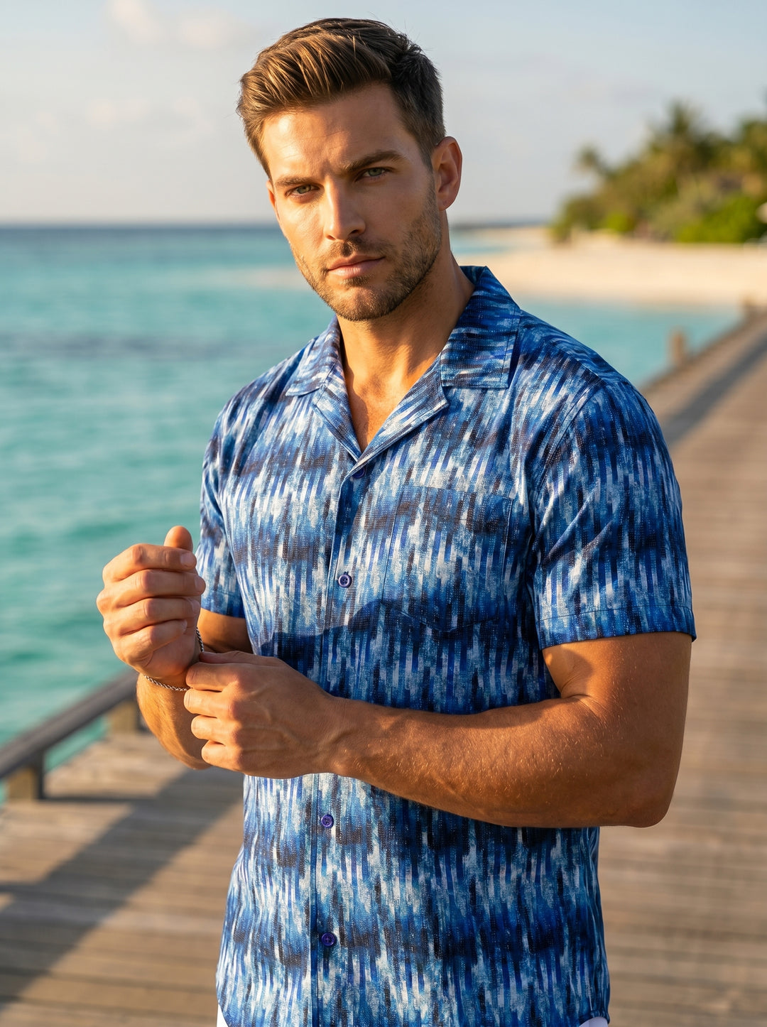 This men's short-sleeve button-down shirt features a vibrant ikat-inspired pattern in various shades of blue and white. It is designed with a classic camp collar, a single chest pocket, and a curved hem, offering a stylish and breathable fit.