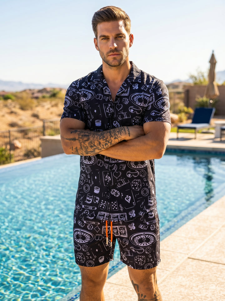 These stylish black swim shorts feature a playful white casino-themed print including roulette wheels, dice, and playing cards. Designed with an elastic waistband and vibrant orange drawstrings, they offer a comfortable fit and a bold, high-contrast look 