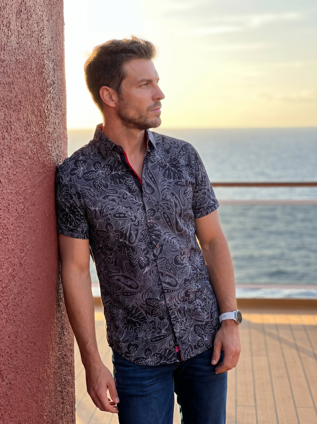 This men's short-sleeve button-down features a sophisticated monochromatic paisley and tropical leaf print on a dark base. Crafted with a tailored fit, it includes a contrasting red inner collar stand and decorative buttons for a refined, modern aesthetic
