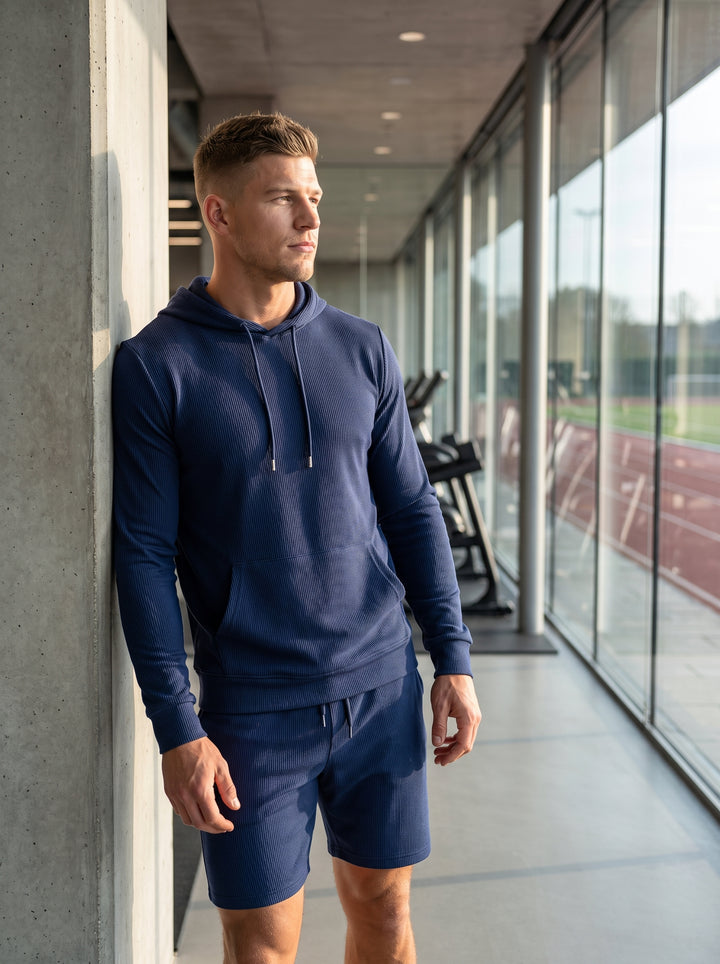 This premium navy performance set features a long-sleeved textured hoodie with a spacious kangaroo pocket and matching technical shorts. Crafted from a breathable ribbed fabric, it offers a streamlined fit designed for both comfort and high-intensity athl