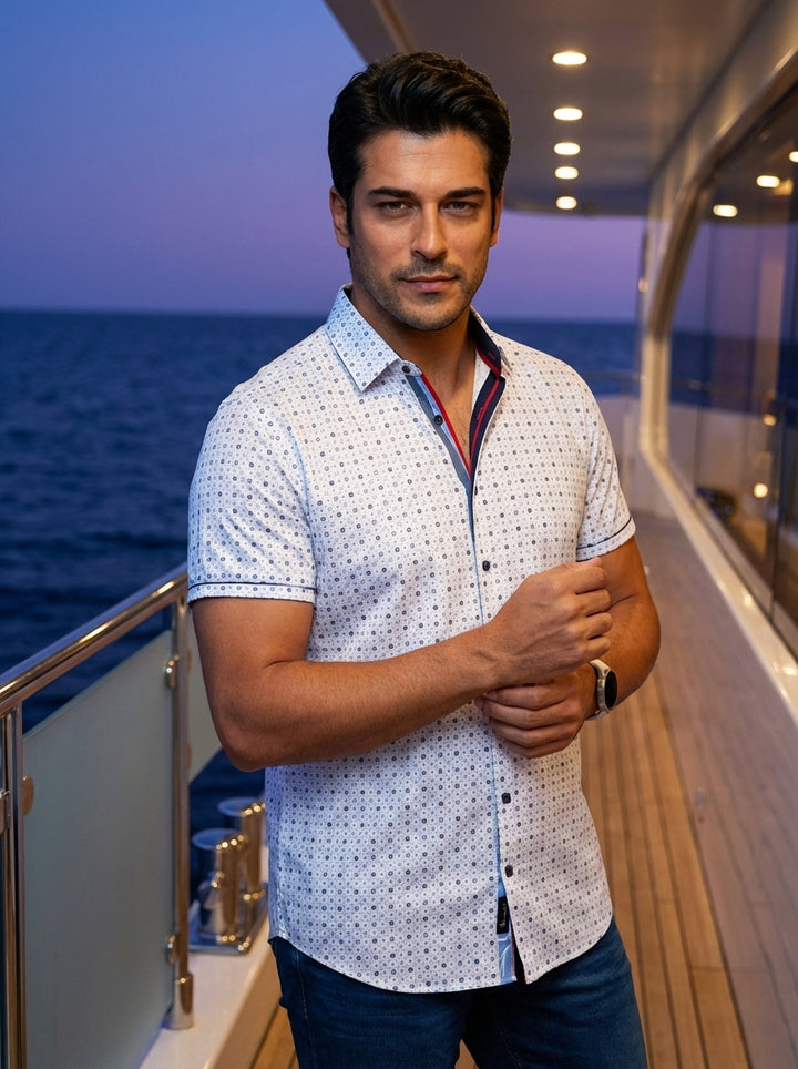 This tailored short-sleeve button-down shirt features a sophisticated white base with a dense geometric micro-print in blue. Contrast detailing along the inner collar and placket adds a modern pop of red and navy, perfect for refined casual summer styling