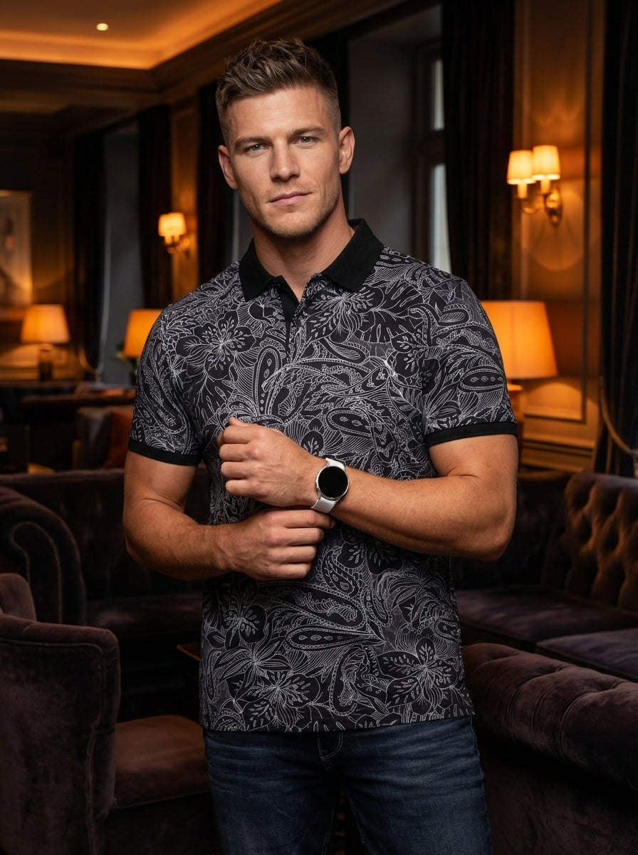 A modern black polo shirt featuring an intricate white floral and paisley line-art print. Designed with a classic solid black collar and sleeve cuffs, this short-sleeved top offers a sophisticated slim fit that blends artistic detail with contemporary mas