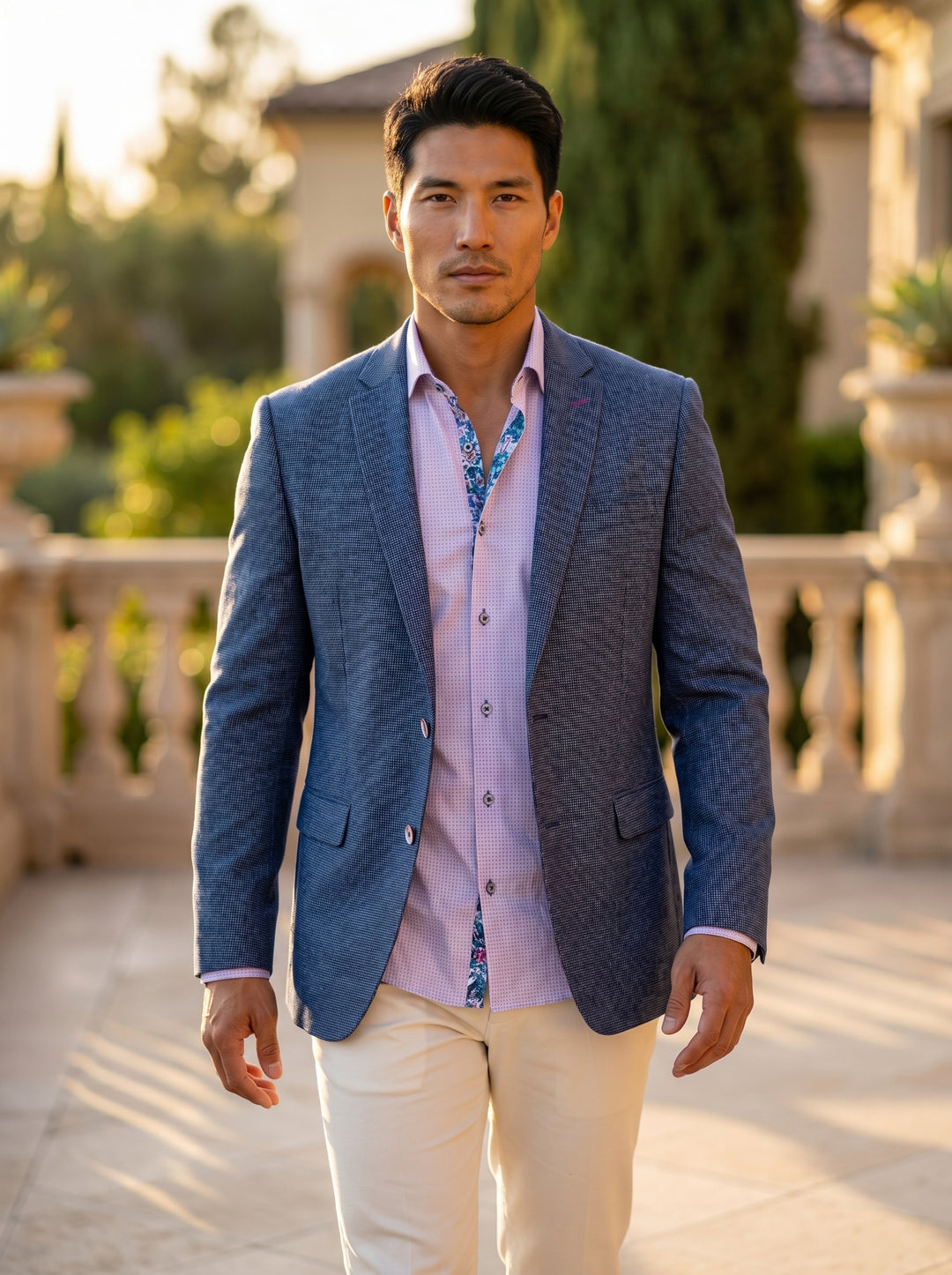 This sophisticated ensemble features a textured blue blazer with subtle micro-patterns, paired with a soft lavender patterned dress shirt showcasing a contrasting floral inner placket. The look is completed with cream-colored trousers, blending classic ta