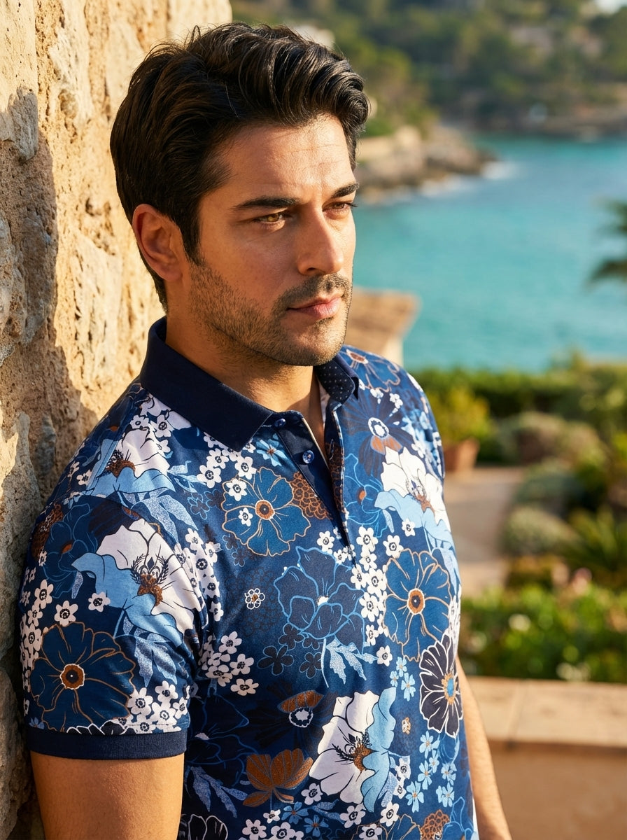 This vibrant men's polo shirt features an intricate botanical print in varying shades of blue, white, and copper. Crafted from a textured fabric, it includes a solid navy spread collar and polished buttons, blending bold floral patterns with a structured 