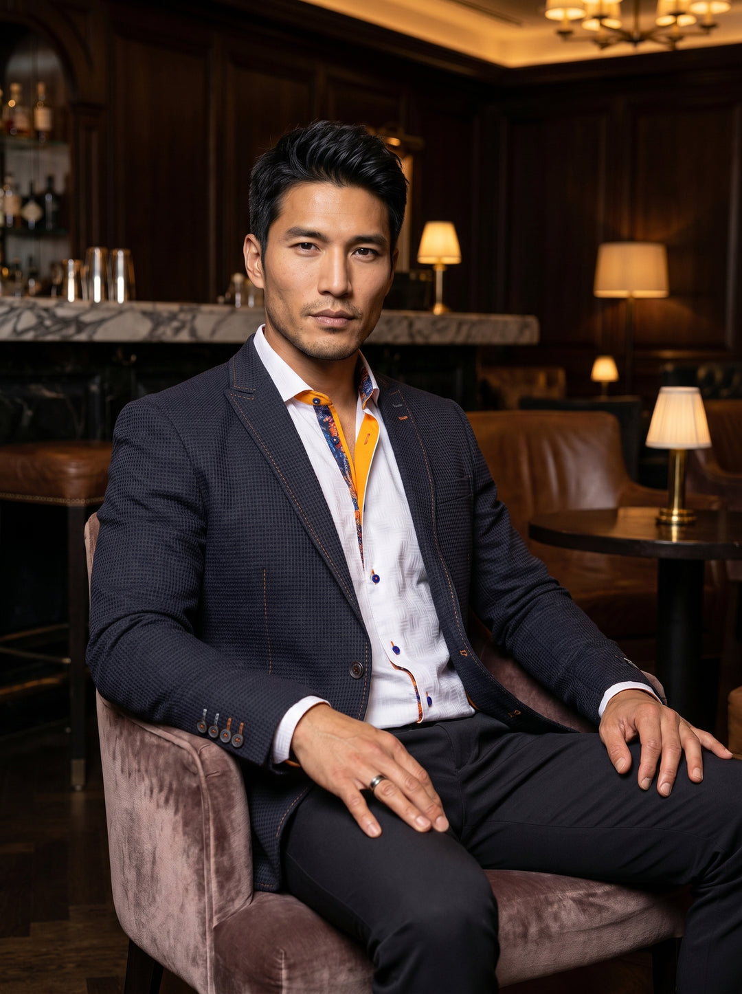 This sophisticated ensemble features a textured navy blazer with notched lapels and orange contrast stitching. It is paired with a white jacquard-weave dress shirt showcasing vibrant orange and blue paisley inner-collar detailing and distinctive blue butt